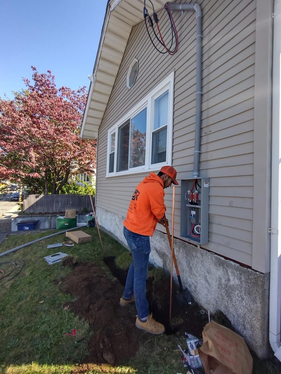 Electrician installing a new meter on the side of a house with landscaping visible.